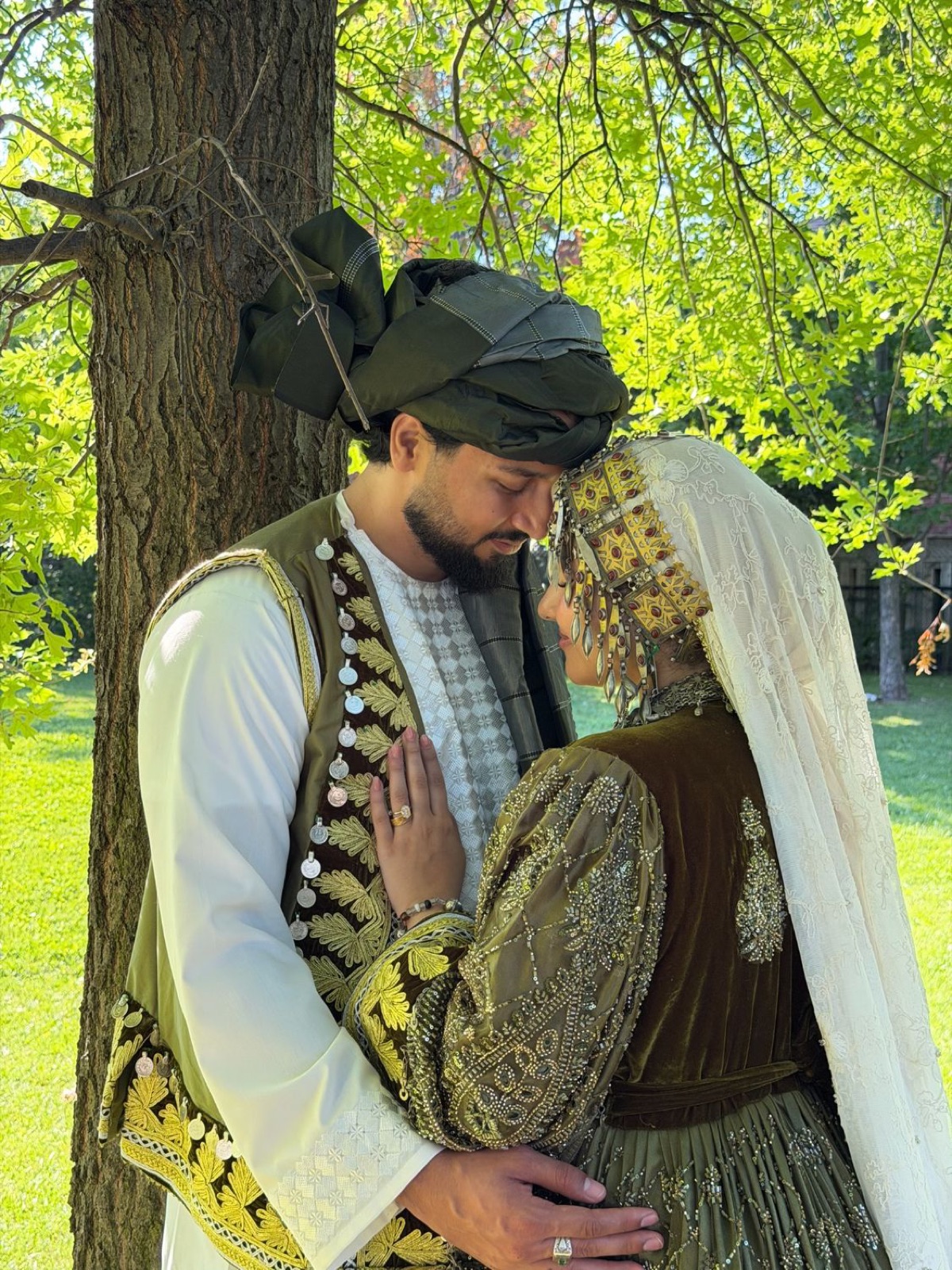 Couple in traditional Afghan wedding dress embracing under a tree